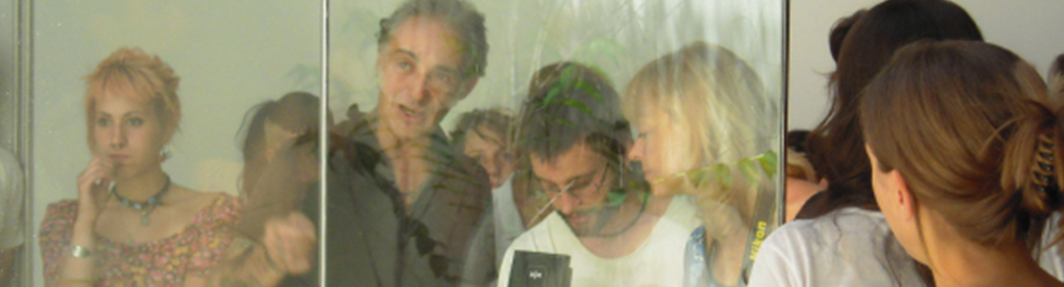 Imagen en la que aparecen varias personas, en particular, se puede observar a un grupo de 3 personas que están realizando una fotografía a través de una cristalera.